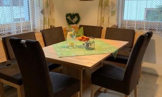 A cozy dining area with a round wooden table and eight chairs. The table is decorated with a tablecloth and there are fruits and drinks ready.