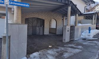 A modern house with a covered entrance and a driveway. The street is covered in snow and the surroundings seem calm.