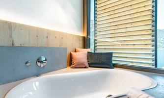 A modern bathroom with a round bathtub and a large window front. Soft cushions on the bathtub cover provide additional comfort.