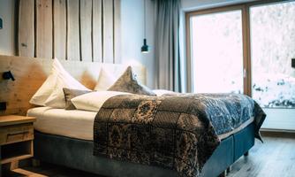 A modern bedroom with a large bed and cozy pillows. The room has large windows that let in plenty of daylight.