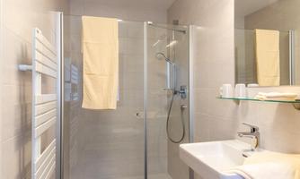 A modern bathroom with a glass shower and a sink. Towels hang on the wall and there are toiletries on the shelf.