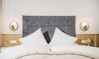 A modern bedroom with a large bed and two pillows. Stylish lamps hang on the wall next to the headboard.