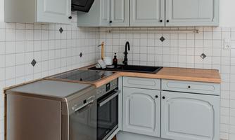 A modern kitchen with gray cabinets and a wood countertop. It is equipped with a stove, a dishwasher, and an elegant black faucet.