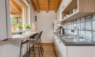 A modern kitchen with a wooden ceiling and large windows. On the countertop are plants and kitchen appliances.
