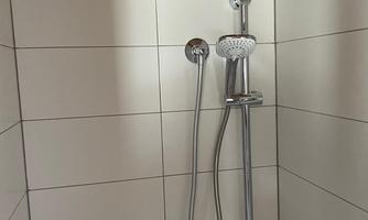 A modern shower with a rain showerhead and a handheld showerhead. The walls are tiled with white tiles.