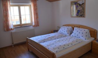 A cozy bedroom with a double bed and white bedding with blue stars. The room has large windows and warm wood design.