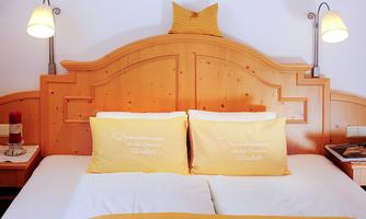 A cozy bedroom with a large bed and yellow pillows. The wooden wall and the lamps create an inviting atmosphere.