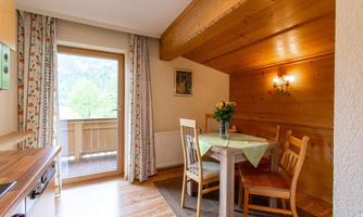 A cozy dining nook with a wooden table and chairs. The room has windows overlooking nature and warm wood paneling.