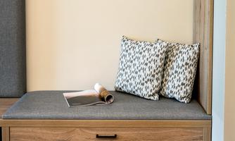 A cozy seating area with two decorative cushions and a magazine on a gray seating surface. The wall behind the seat is painted in neutral tones.