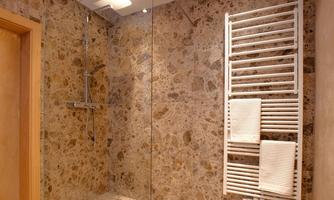 A modern shower with stone walls and a large glass partition. Towels hang on a white towel warmer.