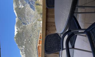 A balcony with a table and chairs. In the background, snow-covered mountains and a blue sky can be seen.