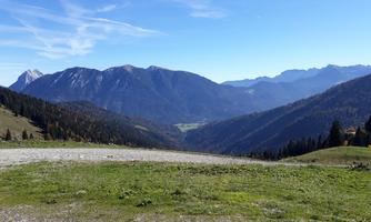 A picturesque mountain landscape with green meadows and high mountains in the background. The sky is clear and blue, perfect for a view of nature.