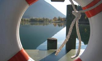 A look through a lifebuoy at a calm lake, surrounded by mountains. The water's surface reflects the landscape.