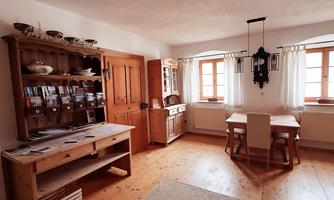 A cozy room with wooden furniture and natural light. A table with chairs and a shelf with decorations are visible.