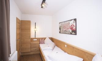 A simple bedroom with two beds and wooden furniture. A decorative picture hangs on the wall, and the room has a bright, modern atmosphere.