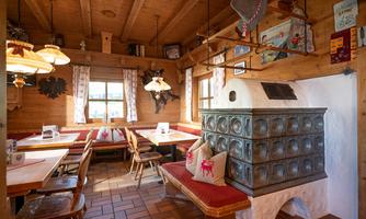 A cozy dining room with wooden furniture and a traditional tiled stove. Large windows provide plenty of daylight.