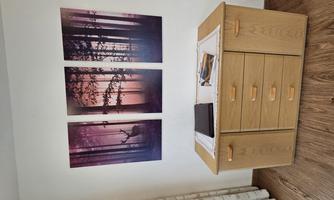 A wooden cabinet with drawers stands against the wall. Above it hang three pictures of a forest with a stag at sunset.