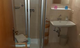 A small bathroom with a shower cabin, a sink, and a toilet. Towels and toiletries are visible.