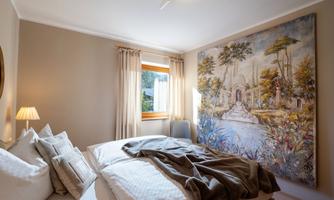 A cozy bedroom with a large bed and soft pillows. A colorful piece of artwork depicting a landscape hangs on the wall.