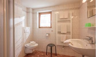 A modern bathroom with white tiles and a sink. There is a shower, towels, and a small stool.