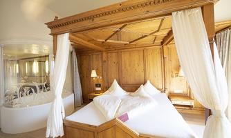 A cozy bedroom with a wooden bed and elegant curtains. In the background, a modern bathroom can be seen.