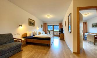 A bright room with a double bed, a seating area, and a large window with a view. The decor is simple and modern, with wooden flooring and soft colors.