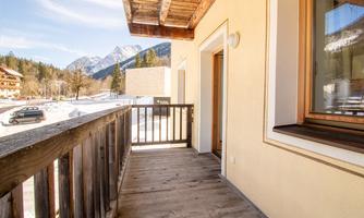 A balcony with a wooden floor and a view of snow-covered mountains. The surroundings are calm and picturesque.