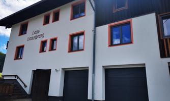 A modern building with a bright white paint and orange window frames. The facade features two garage doors and a clear blue sky in the background.
