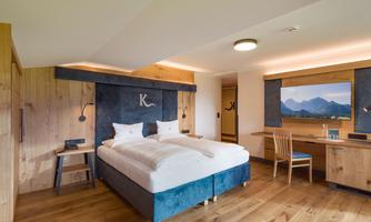 A modern bedroom with a double bed and wooden-clad walls. There is a desk and windows with a view of the mountains.