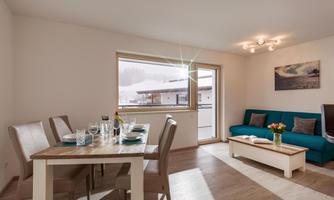 A bright and modern living kitchen with a dining table, a blue sofa, and a beautiful view of the landscape. The room feels cozy and inviting.
