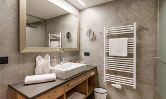 A modern bathroom with a sink and a large mirror. The walls are in a simple gray tone, and there are towels as well as a towel radiator.