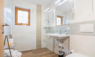 A modern bathroom with a shower, a sink, and a toilet. It has a bright style with wooden floor and a window.