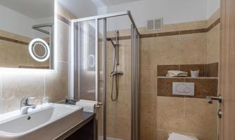 A modern bathroom with a shower and a sink. The walls are tiled in light colors, and there is a large mirror present.