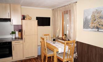 A cozy kitchen with a dining table and wooden chairs. The walls are painted in warm colors, and there is a painting of a tree in winter.