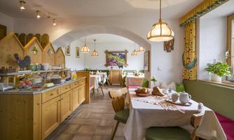 A cozy breakfast room with wooden details.  
Tables are set for guests and a selection of food is visible.