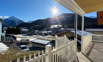 A beautiful view of the mountains and the sun shining over the landscape. In the foreground, a fence and a terrace are visible.