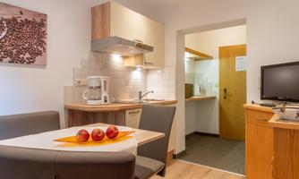 A modern kitchen unit with a dining table and chairs. In the background, another room with a door is visible.