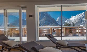 A relaxing room with loungers and a view of snow-covered mountains. Large windows let in plenty of light and provide a beautiful view.
