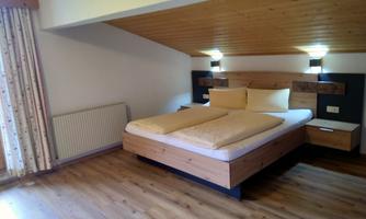 A bright bedroom with a large wooden bed and two pillows. It has a cozy atmosphere and wooden flooring.