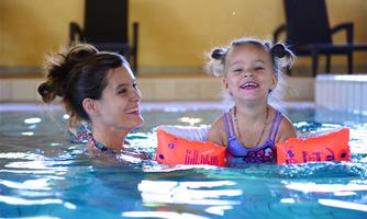 A woman and a little girl are happily smiling in the swimming pool. The girl is wearing floaties and enjoying the water.