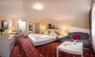 An inviting hotel room with a double bed and a cozy seating area. The warm colors and pleasant lighting create a relaxing atmosphere.