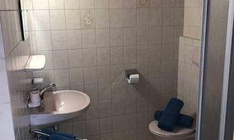 A simple bathroom with white tiles. There is a sink, a toilet, and some blue towels.
