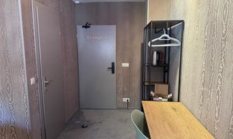 A simple room with a desk, a chair, and a clothes rack. The walls are painted in neutral colors, and the door has the inscription "Shanghai".