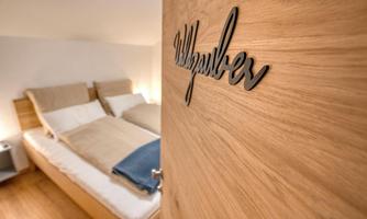A cozy bedroom with wooden decor and an inviting bed. The door bears the inscription "Welcome".