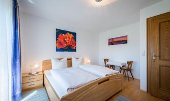 A bright bedroom with two beds and colorful pictures on the wall. A small dining area with a table and chairs is also available.