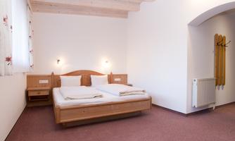A simple room with a double bed and two nightstands. The walls are light, and there is a small radiator as well as a wardrobe.