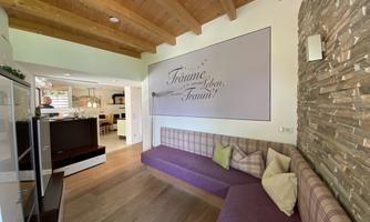 A modern kitchen with wooden ceilings and a cozy seating area. A decorative inscription hangs on the wall.