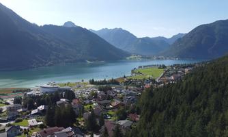A picturesque landscape with a lake and majestic mountains in the background. The surroundings are green and showcase a typical village with houses.