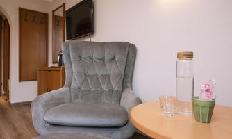 A cozy armchair stands next to a small table. On the table are a water bottle, a glass, and a plant pot.
