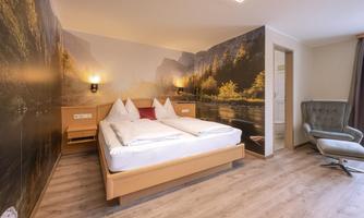A modern hotel room with a double bed and elegant decor. On the wall, there is a picturesque landscape painting that creates a tranquil atmosphere.